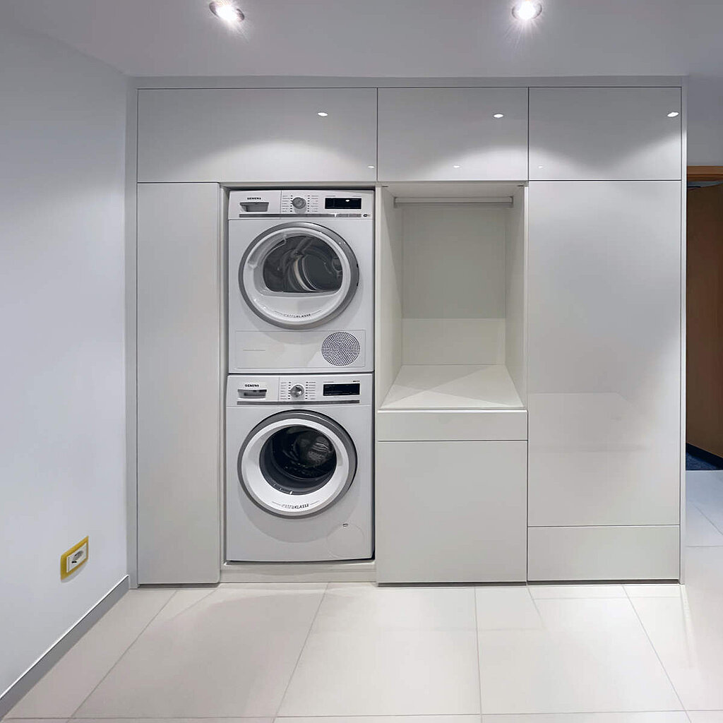 Diese Lösung für den Hauswirtschaftsraum bringt Ordnung in den Alltag. Waschmaschine und Trockner sind ergonomisch in die Schrankwand integriert. Die Hochglanz-Fronten wirken sauber und modern. Neben den Geräten bietet ein offenes Fach mit Kleiderstange Platz zum Trocknen oder Vorbereiten der Wäsche, während die umliegenden Schränke sämtliche Utensilien unsichtbar verstauen.
