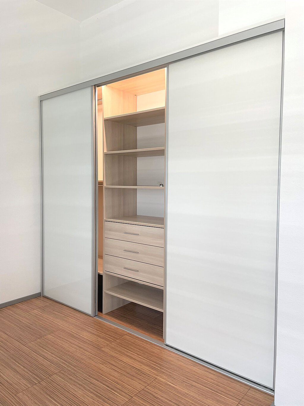 Die Kombination von weißen Schiebetüren und einem Innensystem aus Holz macht den Einbauschrank zum schönen Hingucker im Schlafzimmer.