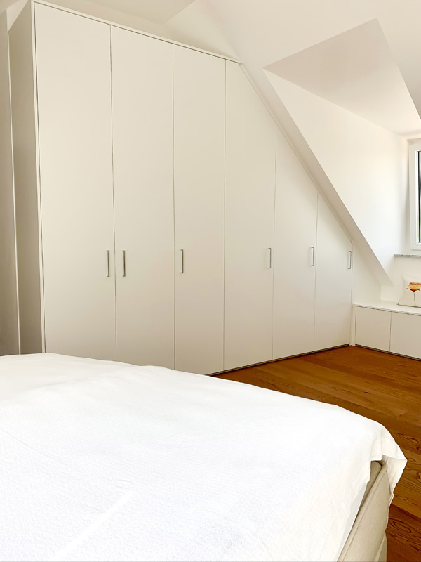 Weißes Schranksystem für das Schlafzimmer unter einer Dachschräge verbaut